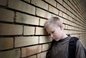 Sad bullied boy leaning on a wall